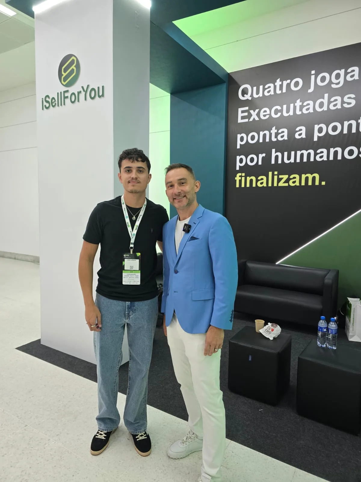 Two men posing in front of the iSellForYou wall and logo at an Afiliados Brasil expo stand
