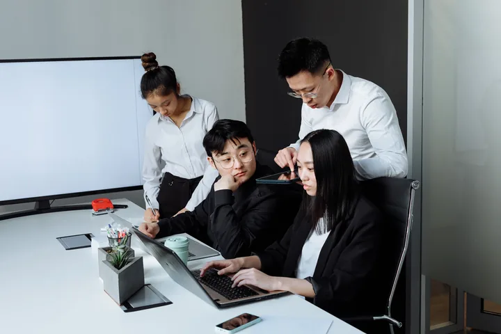 Equipe de profissionais asiáticos reunida em volta de um notebook em sala de reunião, contexto de tradução de chinês