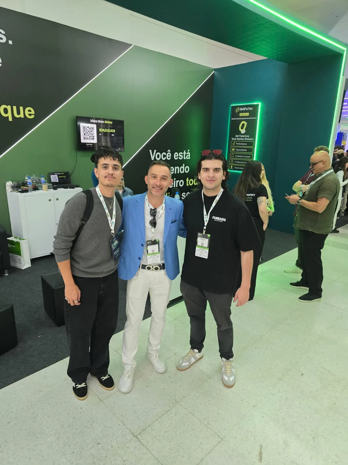 Three men posing together in front of the iSellForYou stand at the Afiliados Brasil expo in São Paulo