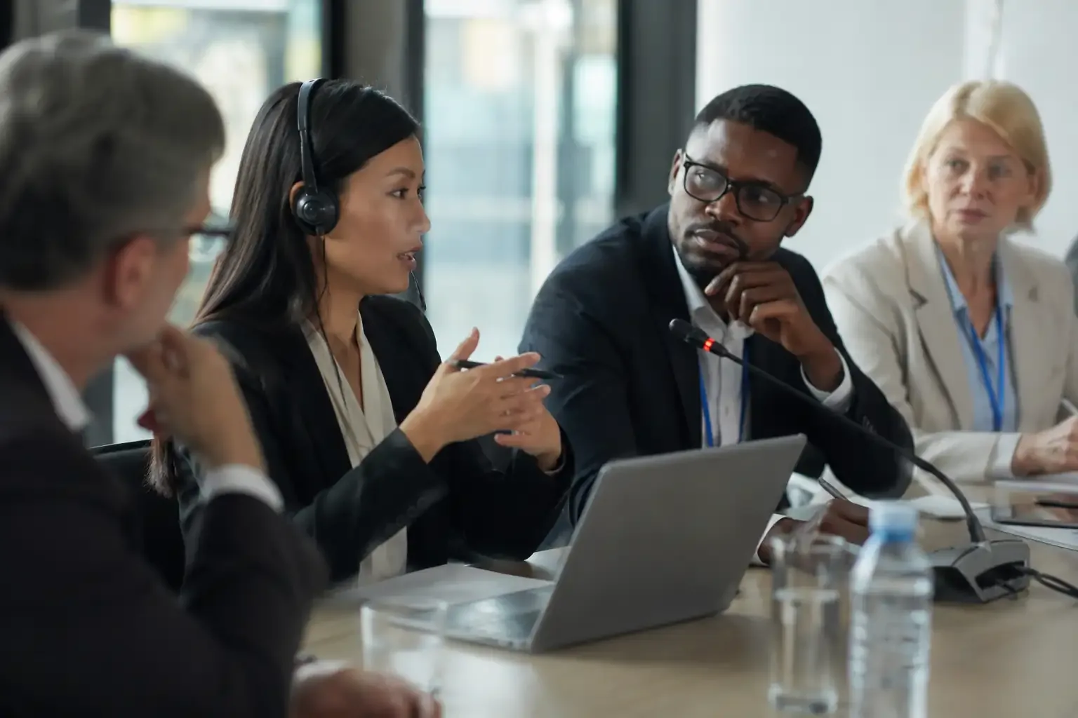 Intérprete de fone de ouvido falando a participantes de uma reunião internacional, com microfone e notebook sobre a mesa