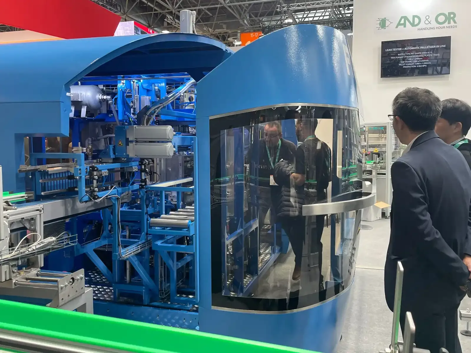 Visitante observa máquina industrial azul em estande de feira de plásticos na K 2025, na Alemanha
