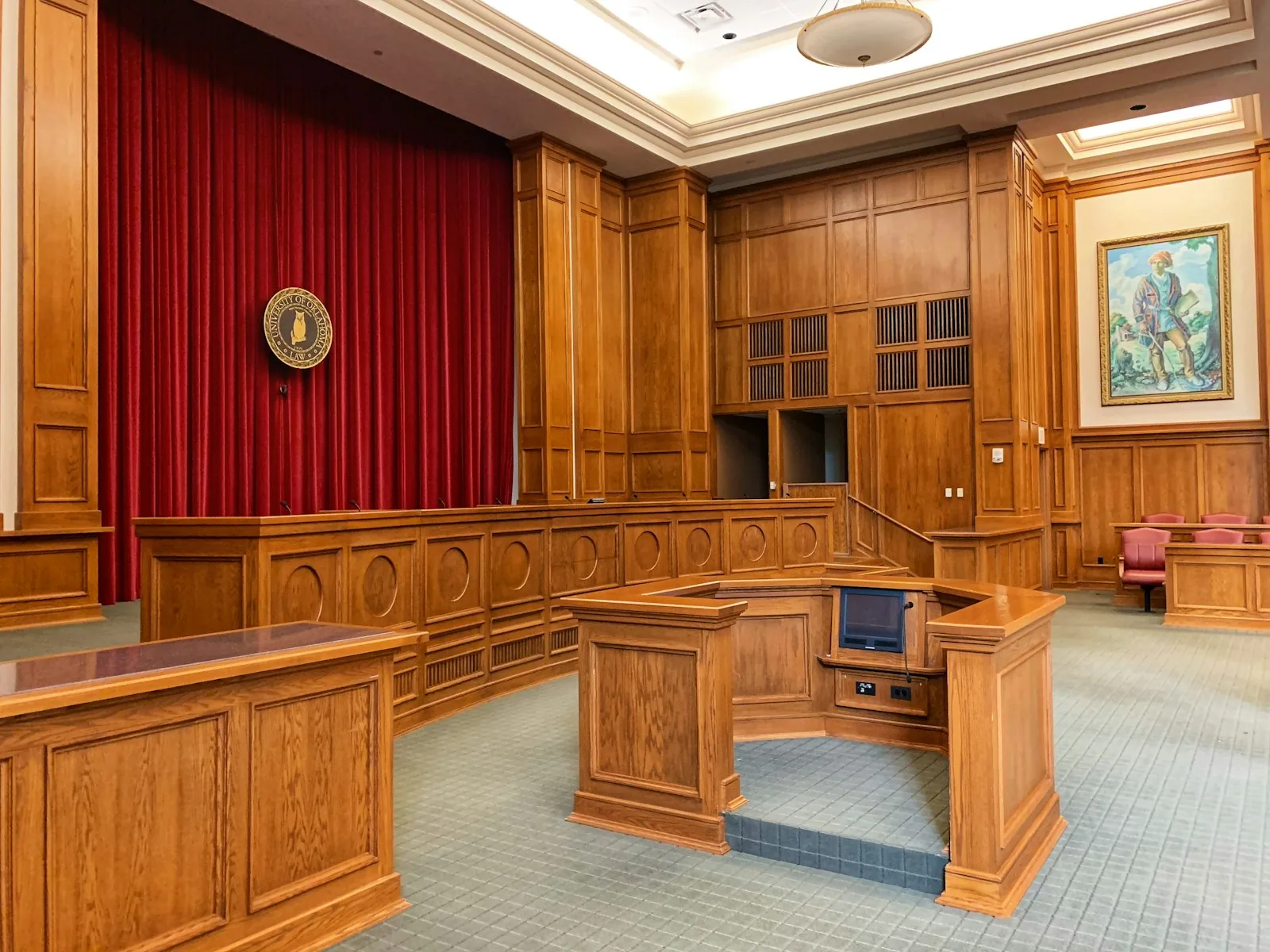 Sala de tribunal com bancada de madeira, cortina vermelha e brasão na parede, cenário de audiência judicial